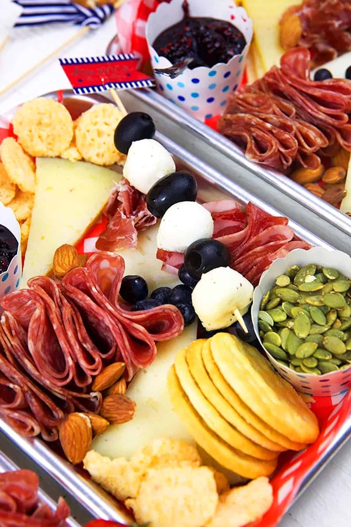 Close up of crackers and charcuterie items on a stainless steel tray.