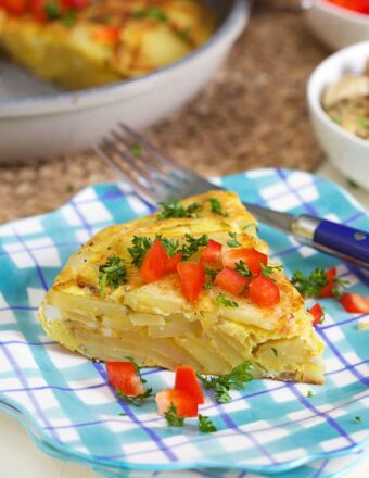 Spanish Tortilla slice on a plaid plate with bell pepper on top.