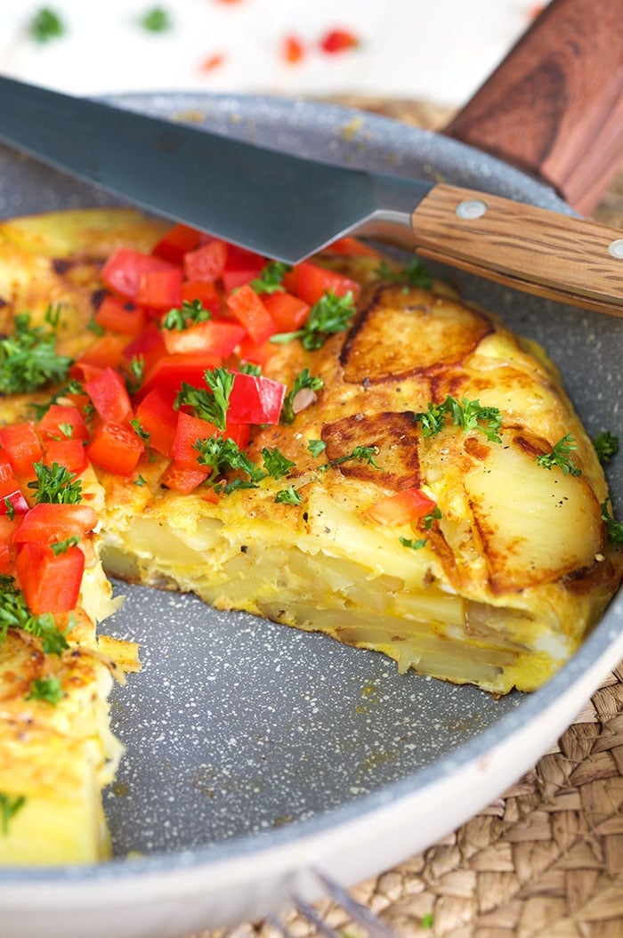 Spanish omelette in a skillet with a slice take out and a knife on top of the skillet.