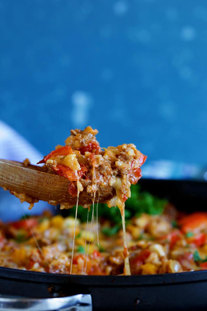 Stuffed pepper casserole being served with a wooden spoon with cheese dripping off the spoon.