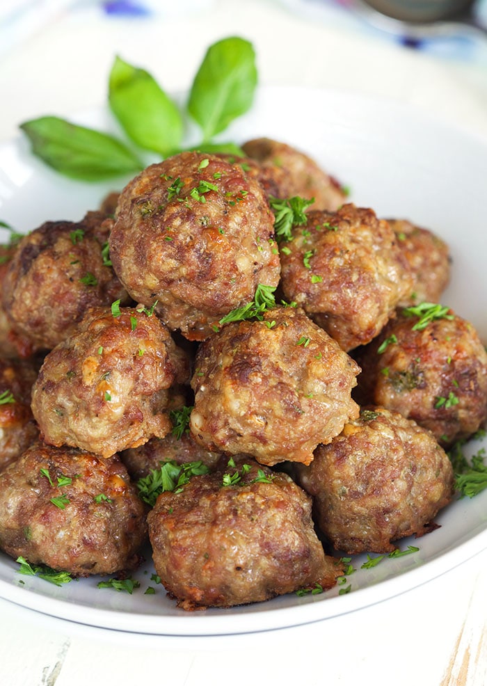 Oven baked meatballs in a white bowl with a leaf of basil.