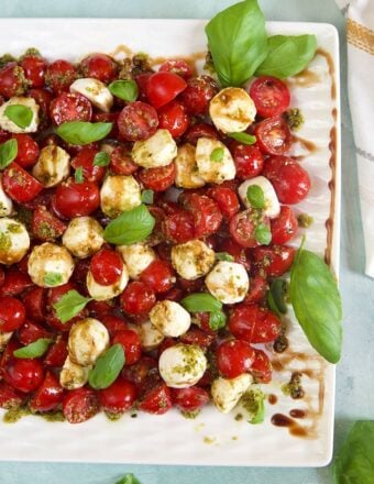 Overhead shot of caprese Salad with cherry tomatoes on a white platter with basil leaves.