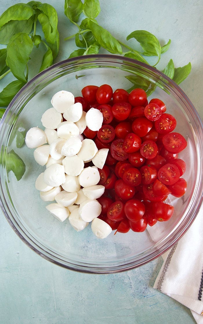 overhead shot of mozzarella and cherry tomatoes in a bowl on a blue background.