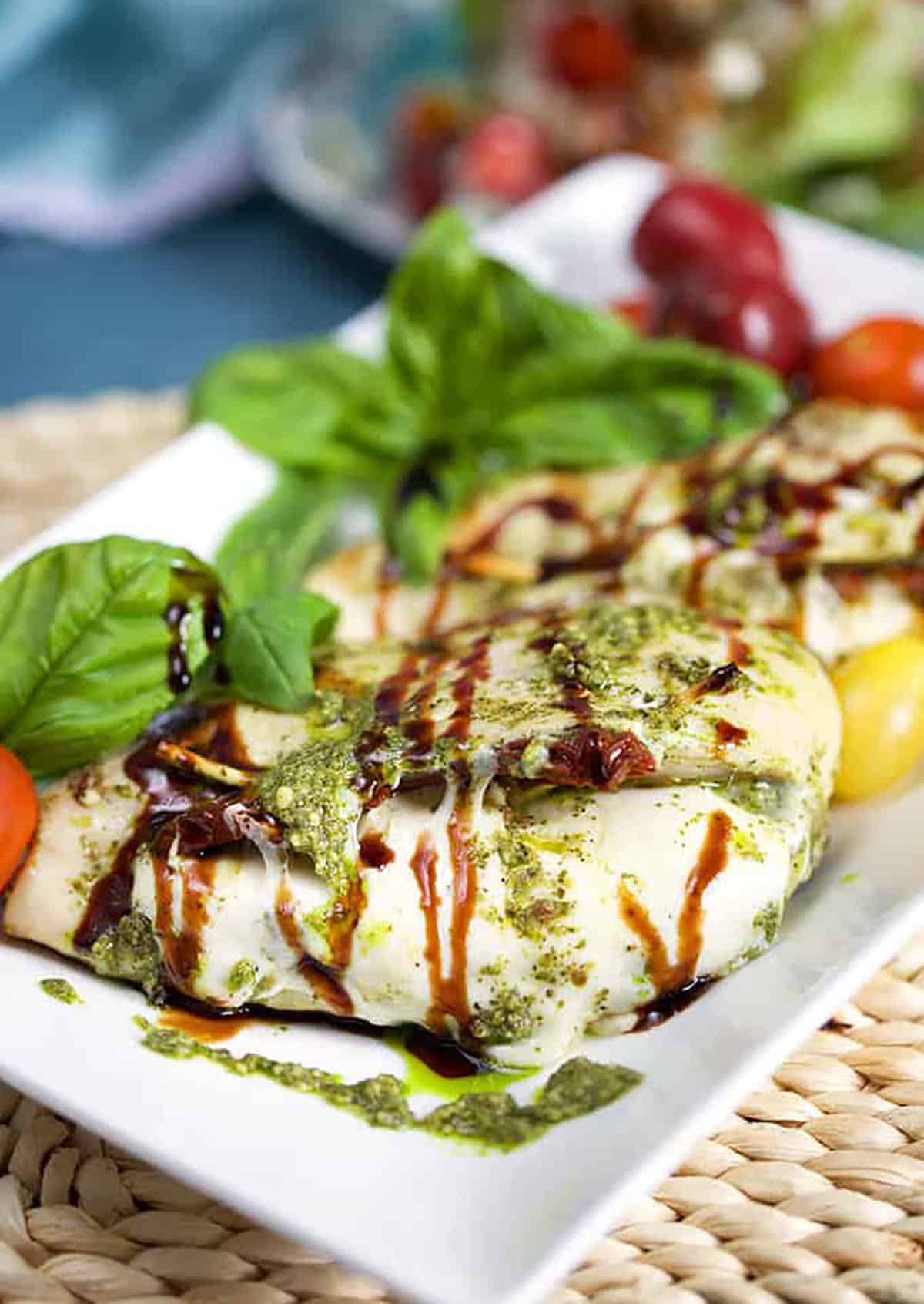 Grilled Caprese Stuffed Chicken on a white platter with fresh basil and tomatoes 