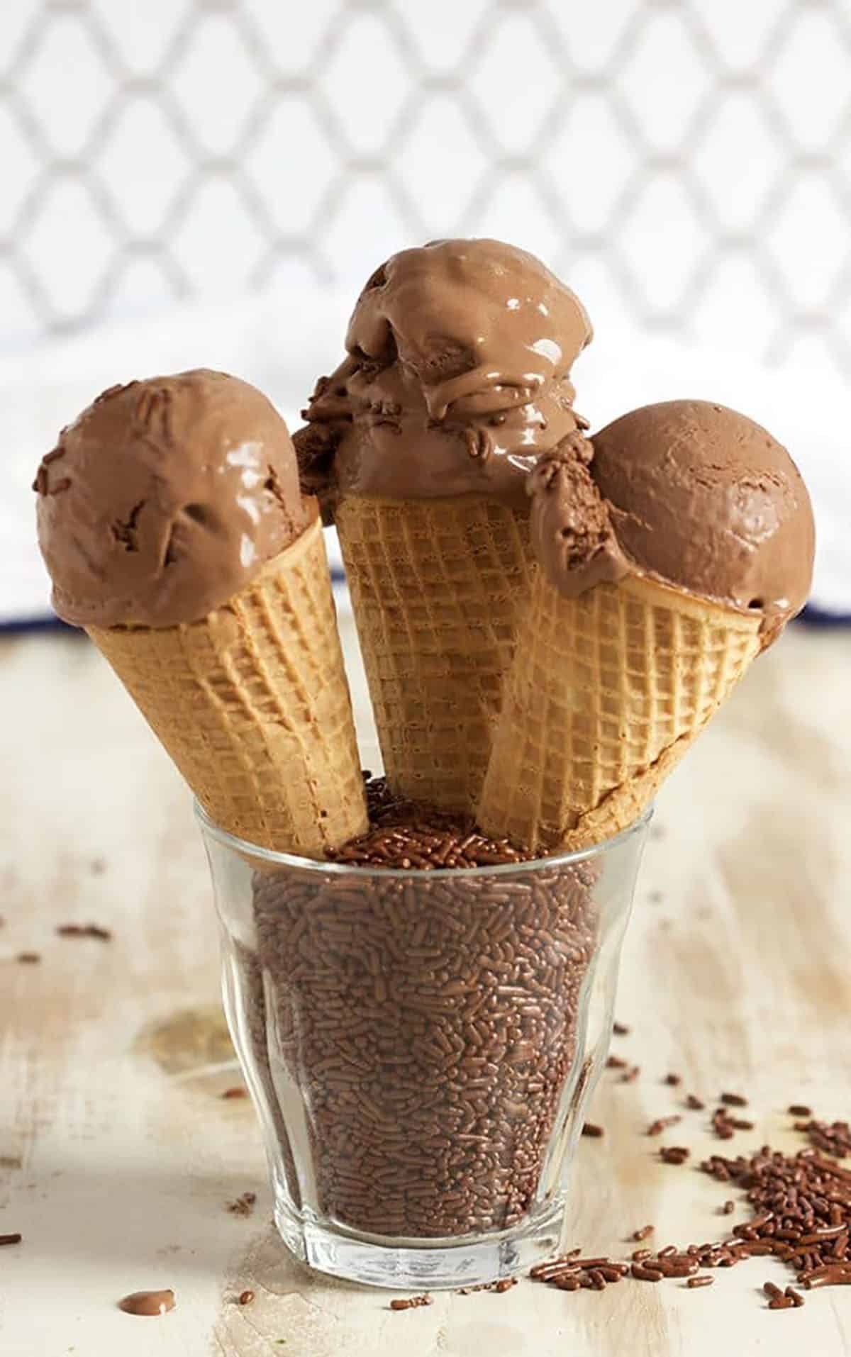 Three cones of chocolate ice cream propped in a glass with chocolate sprinkles.