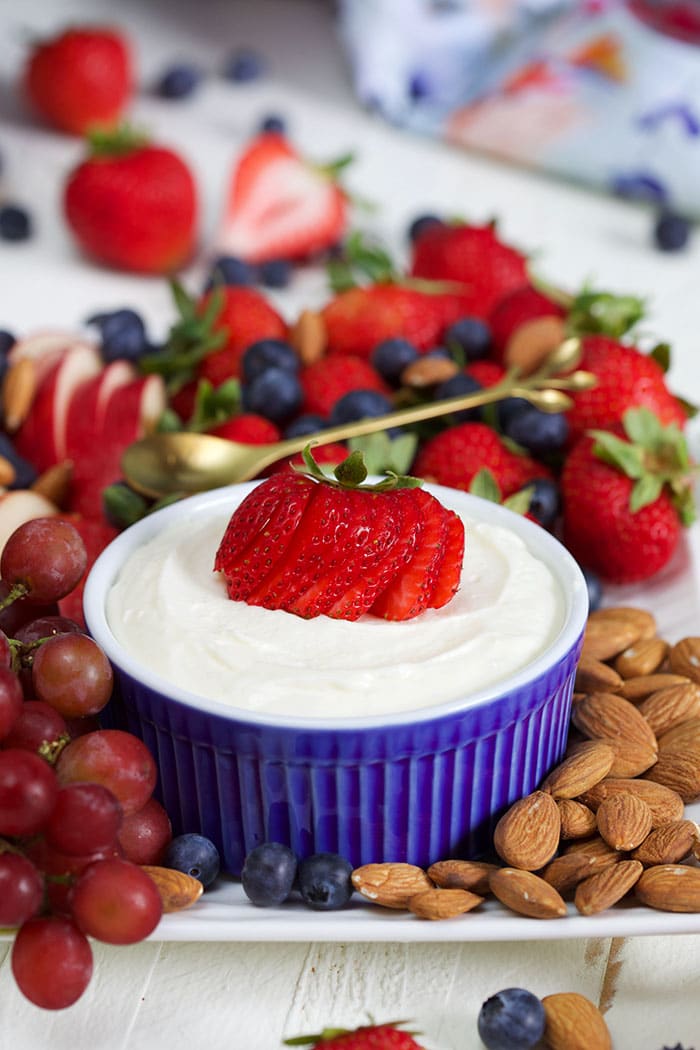 Marshmallow fruit dip in a blue bowl on a white platter with fresh berries, grapes and almonds.
