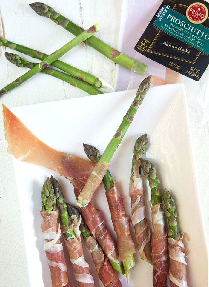 asparagus being wrapped with prosciutto