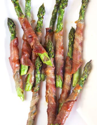 Overhead shot of prosciutto wrapped asparagus on a white platter.