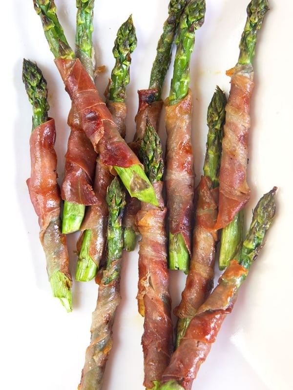 Overhead shot of prosciutto wrapped asparagus on a white platter.