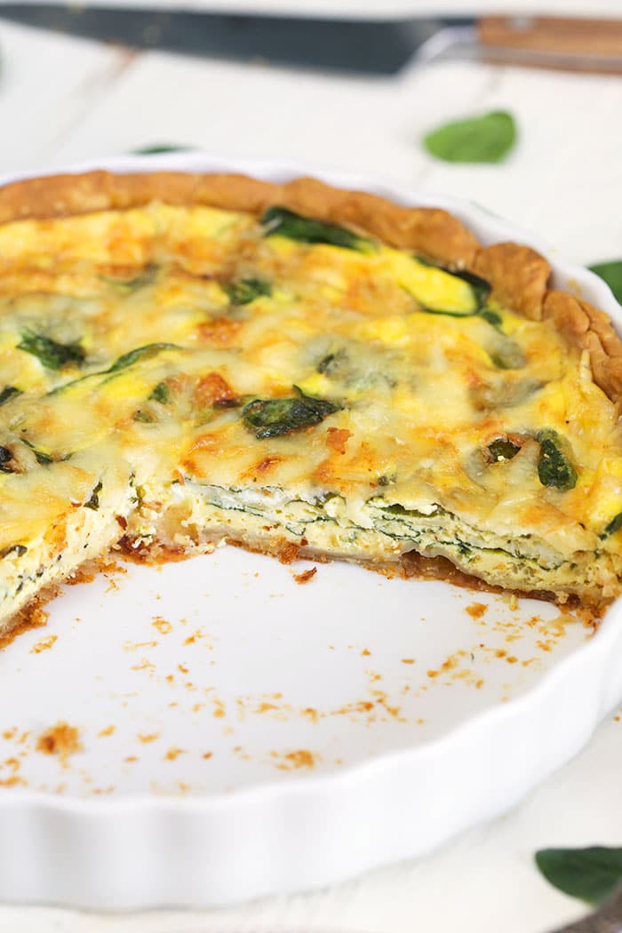 Quiche Florentine in a white pie plate with a slice cut out of it.