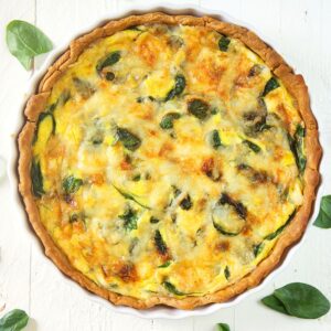 Overhead shot of Quiche Florentine on a white background with spinach leaves around it.