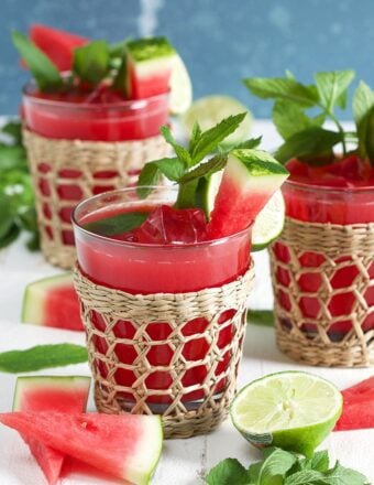 Three watermelon agua frescas in a seagrass glass with watermelon on a white background.