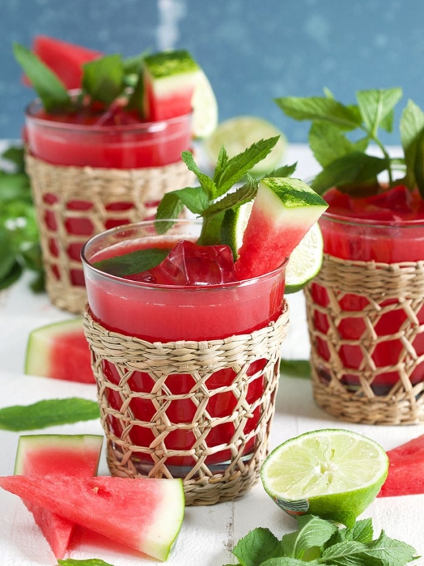 Three watermelon agua frescas in a seagrass glass with watermelon on a white background.