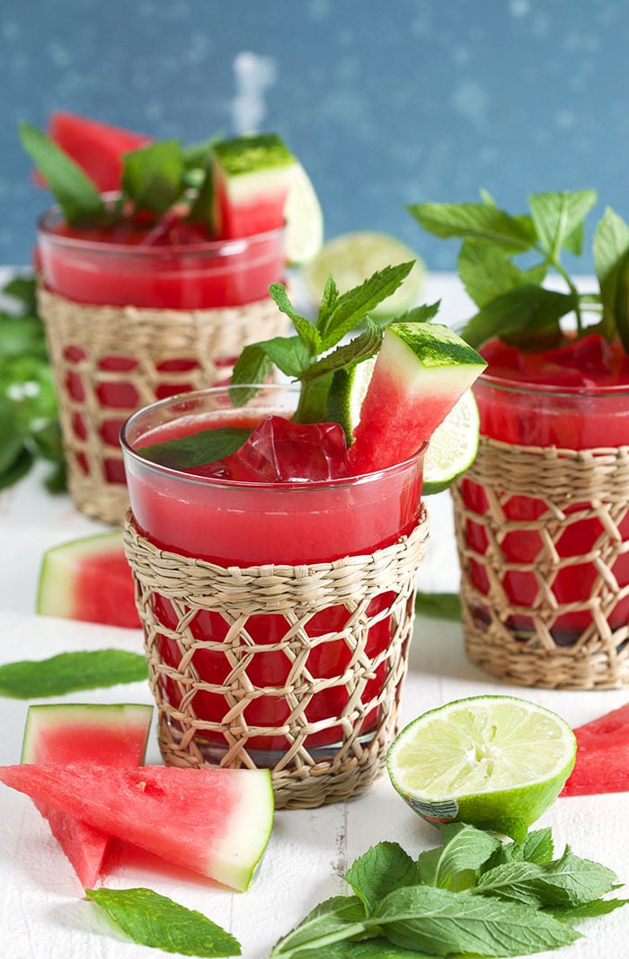 Three watermelon agua frescas in a seagrass glass with watermelon on a white background.