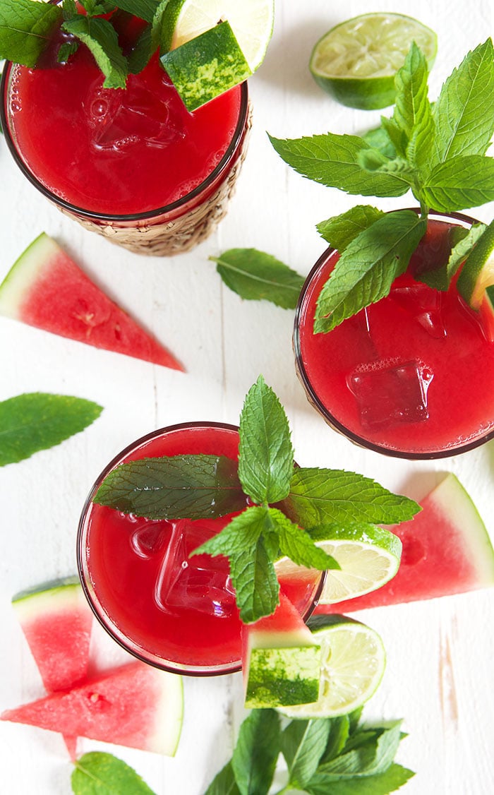 Overhead shot of watermelon agua frescas in three glasses on a white background.