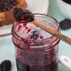 A jar is half filled with blackberry jam.
