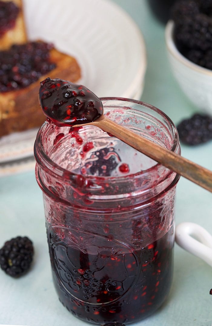 A jar is half filled with blackberry jam. 