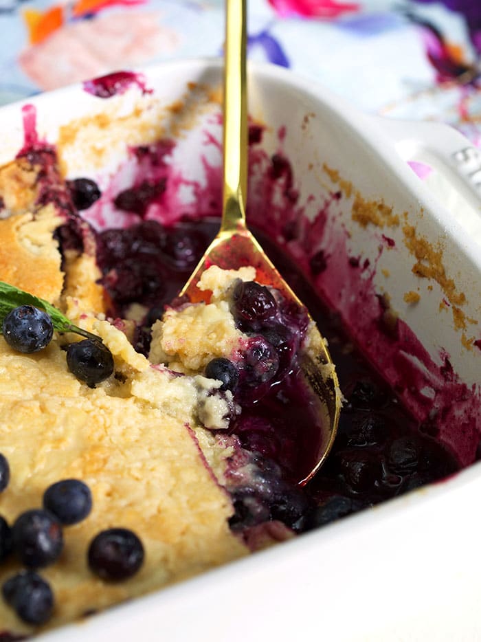 Blueberry Dump Cake in a white baking dish with a gold spoon.
