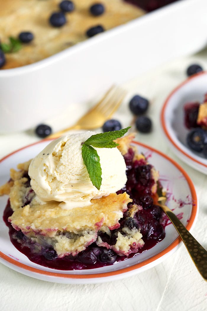 blueberry dump cake on a white plate with a scoop of ice cream and a gold fork.