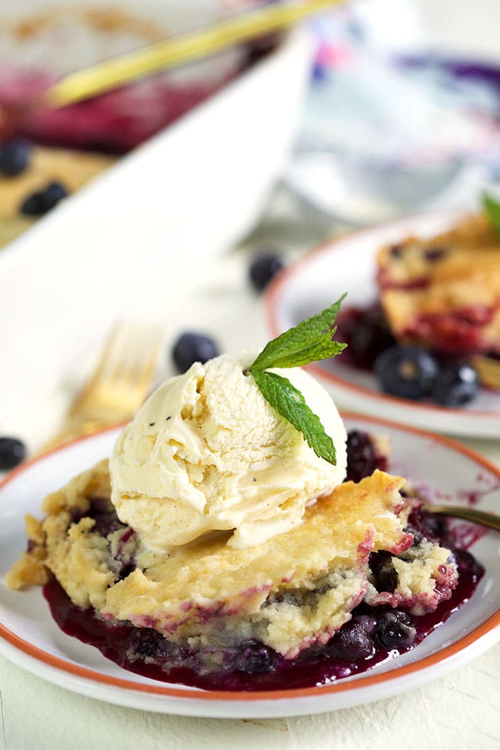Blueberry dump cake on a white plate with a scoop of vanilla ice cream.