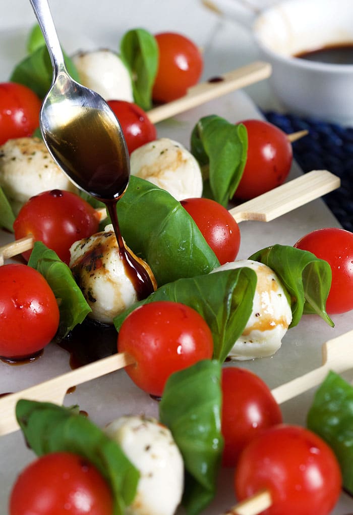 Caprese Skewers on a white board with balsamic glaze being drizzled on them.