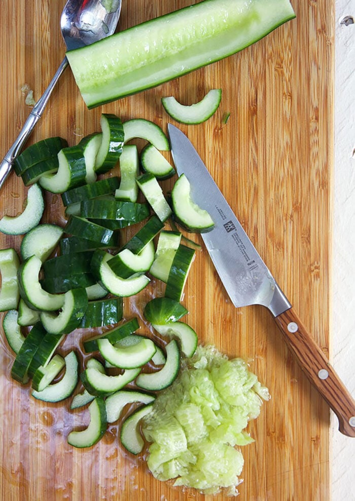 sliced cucumbers on a bamboo cutting board with a knife.