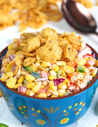 Frito Corn Salad in a blue bowl on a white background with Fritos in the background.