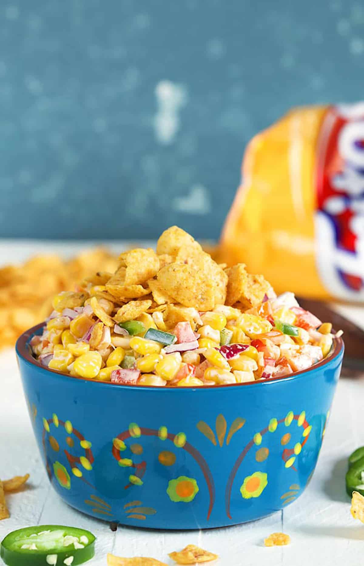 FritoCorn Salad in a blue terra cotta bowl with a bag of Fritos in the background.