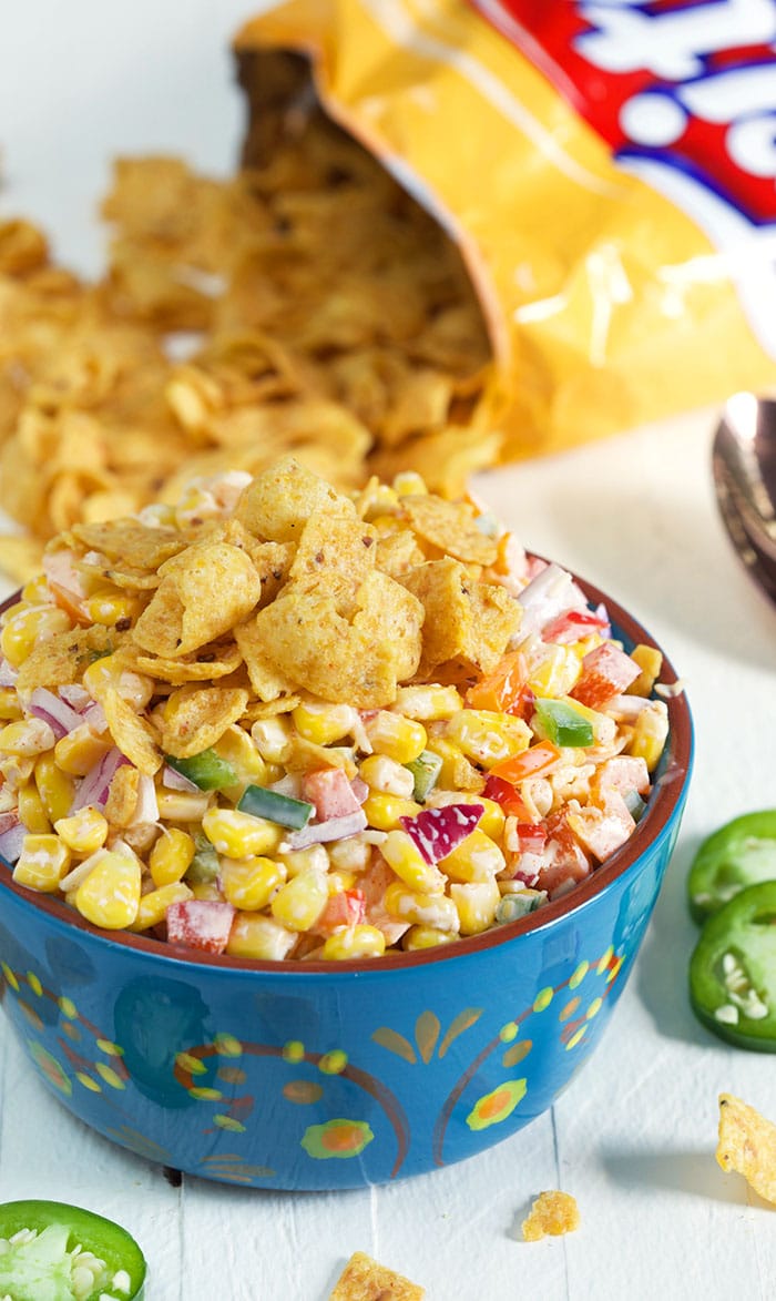 Frito Corn Salad in a blue bowl on a white background with Fritos in the background.