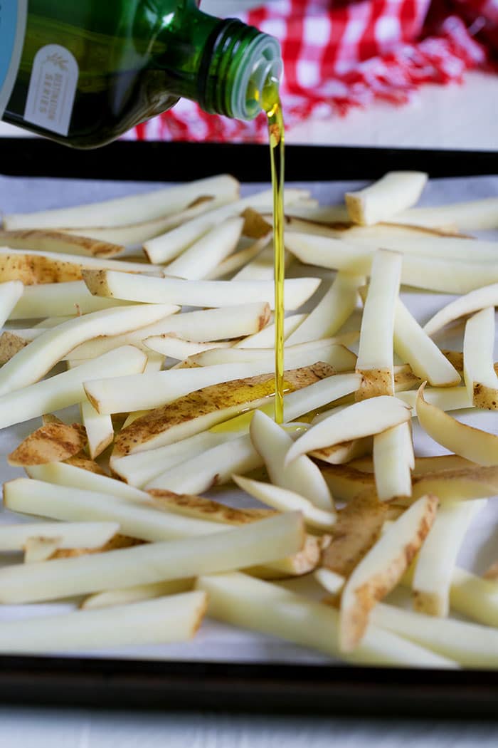 olive oil being drizzled on French fries on baking sheet.