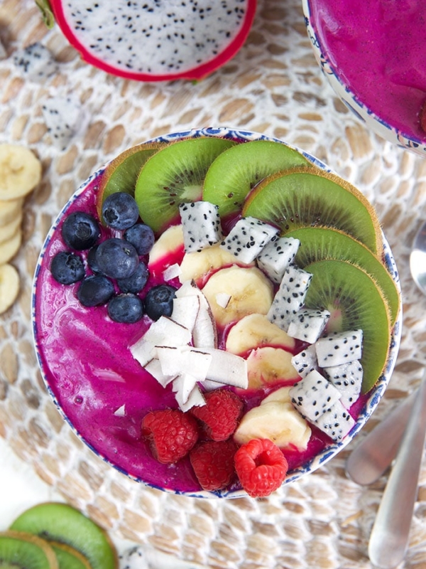 overhead shot of pitaya bowl smoothie bowl with blueberries, kiwi, coconut and raspberries.