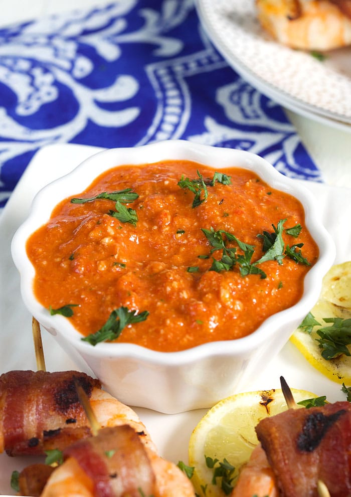 Romesco sauce in a white bowl with a blue and white napkin in the background.