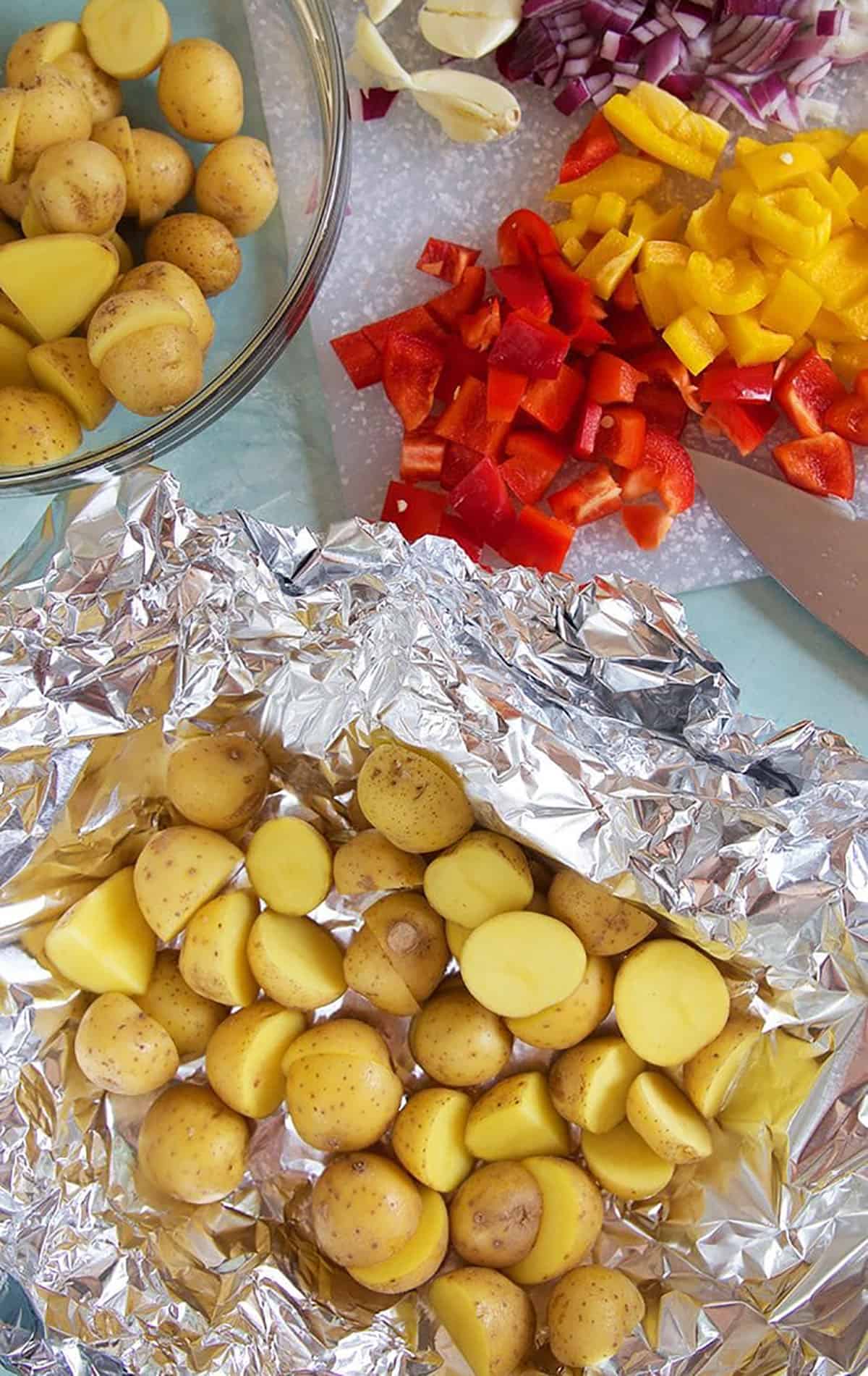 Potatoes in a foil packet with peppers and onions on the side getting ready to be tossed together.