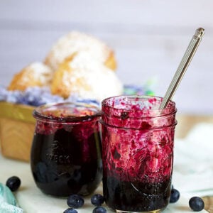 Jars of homemade blueberry jam with a basket of biscuits in the background