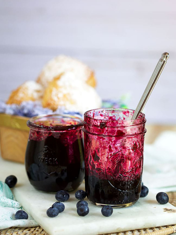 Jars of homemade blueberry jam with a basket of biscuits in the background