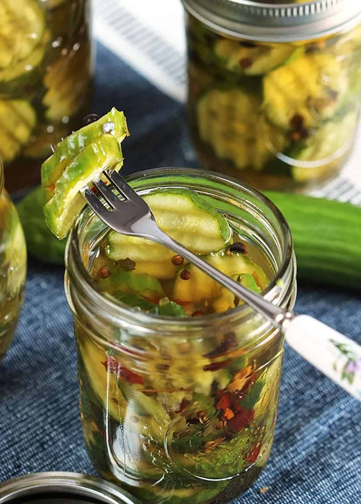 Bread and Butter Pickle on a fork propped on the top of a jar of pickles.