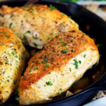 Cast Iron skillet chicken breasts in a cast iron skillet with a blue plate in the front.