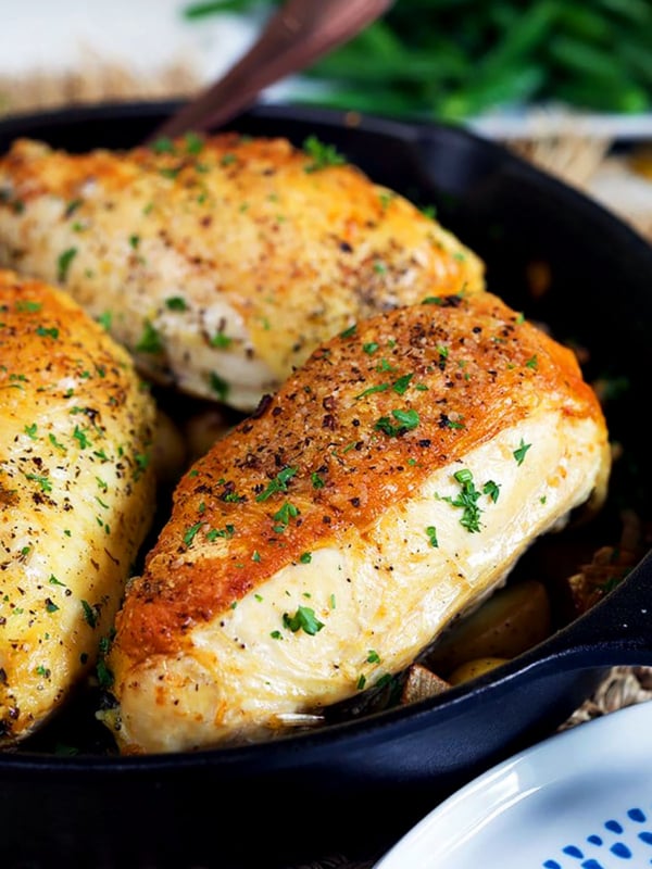 Cast Iron skillet chicken breasts in a cast iron skillet with a blue plate in the front.