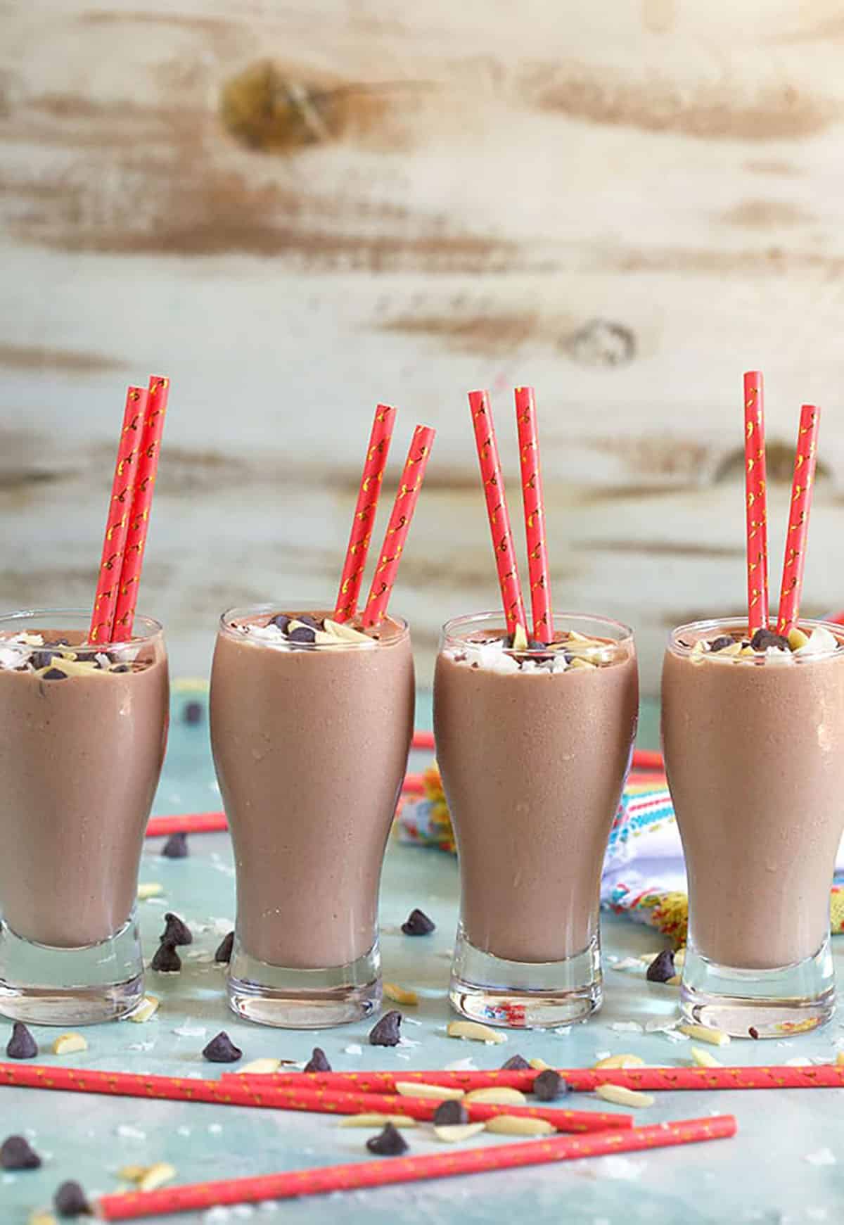 Four glasses of Chocolate Banana Smoothies on a blue background with a coral colored paper straw.