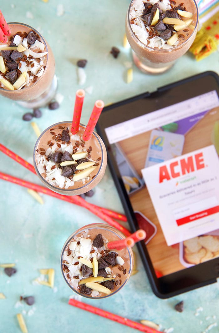 Overhead shot of four chocolate banana smoothies on a blue background with an iPad with the ACME shopping app loaded.
