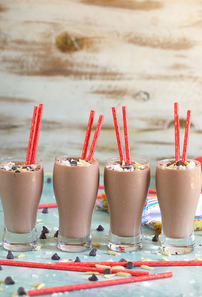 Four glasses of Chocolate Banana Smoothies on a blue background with a coral colored paper straw.