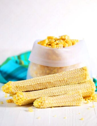 Corn off the cob in a freezer bag with cobs stacked in front.