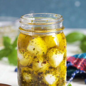 Marinated Mozzarella Balls in a jar with olive oil on a white background with basil leaves.