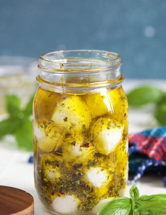 Marinated Mozzarella Balls in a jar with olive oil on a white background with basil leaves.