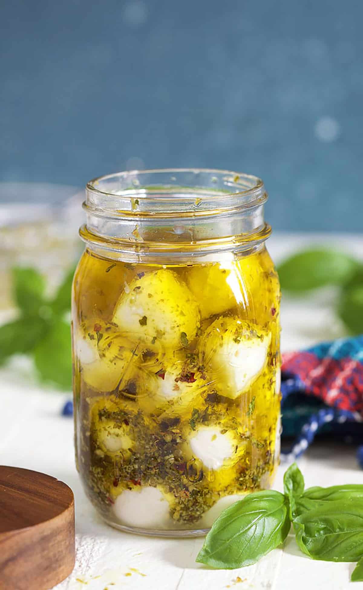 Marinated Mozzarella Balls in a jar with olive oil on a white background with basil leaves.