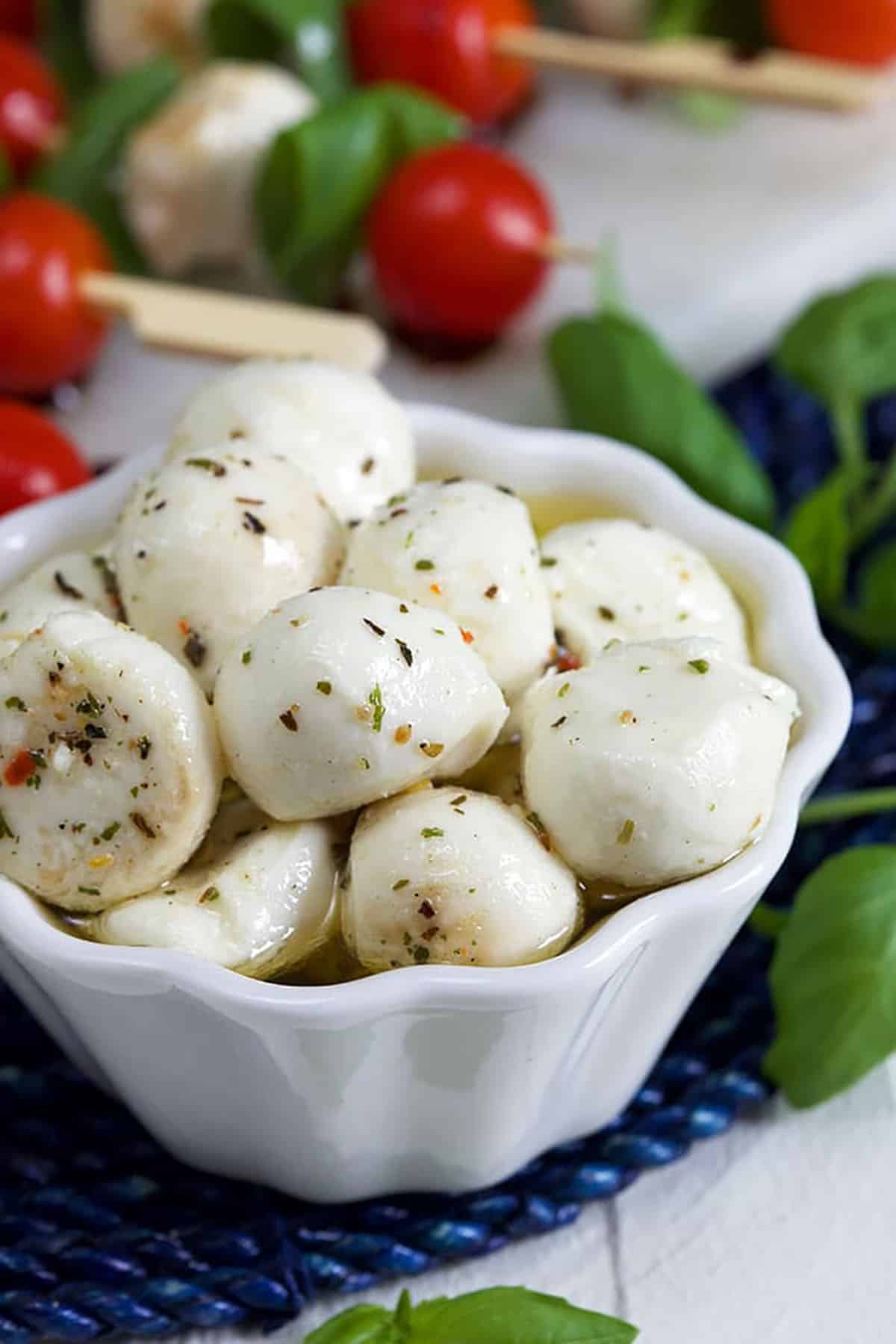 Marinated mozzarella balls in a white dish on a blue placemat.