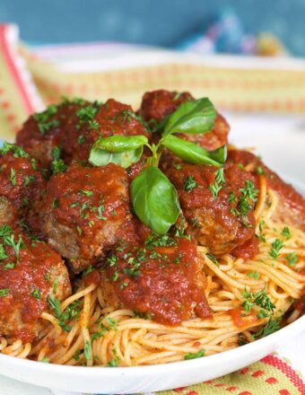 Fried Meatballs on a pile of spaghetti with tomato sauce in a white bowl.
