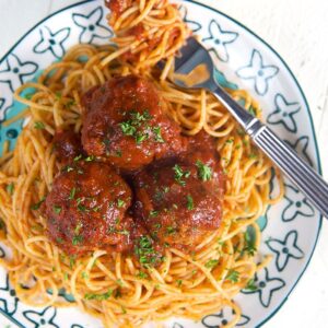 Overhead shot of spaghetti and meatballs on a white plate with a turquoise design and a fork with spaghetti swirled around it.