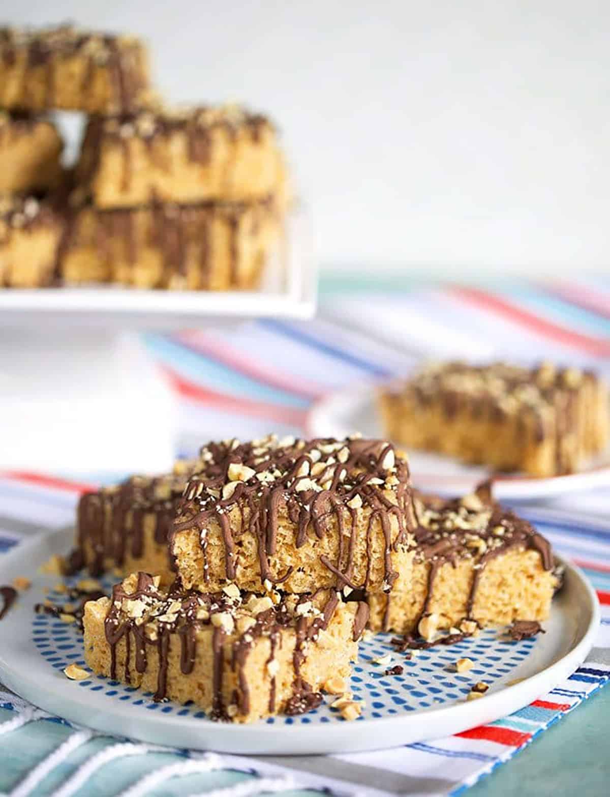 Chocolate Peanut Butter Rice Krispie treats on a plate with a cake plate in the background.