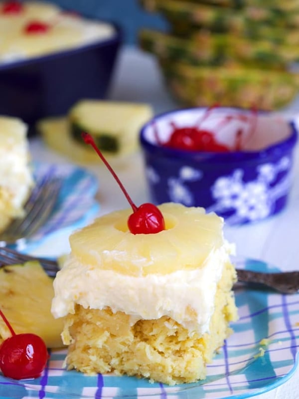 Pineapple Sunshine Cake on a plaid plate with pineapple and a cherry on top.